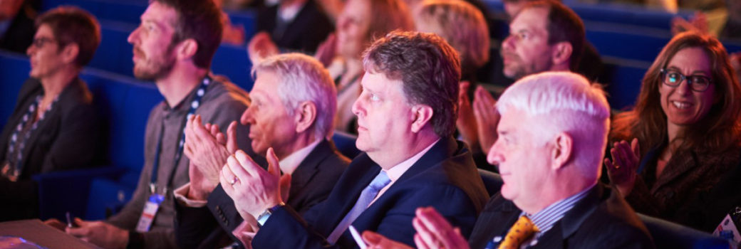 An image of men in a theatre style audience applauding