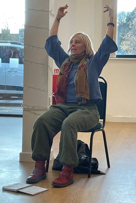 A picture of a Pain Cafe facilitator sat in a chair showing movement techniques to improve pain