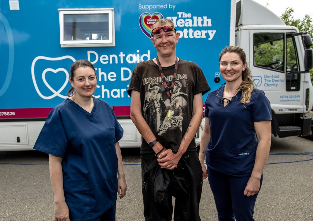 A photo of two dental nurses and a patient stood outside the Dentaid mobile clinic unit