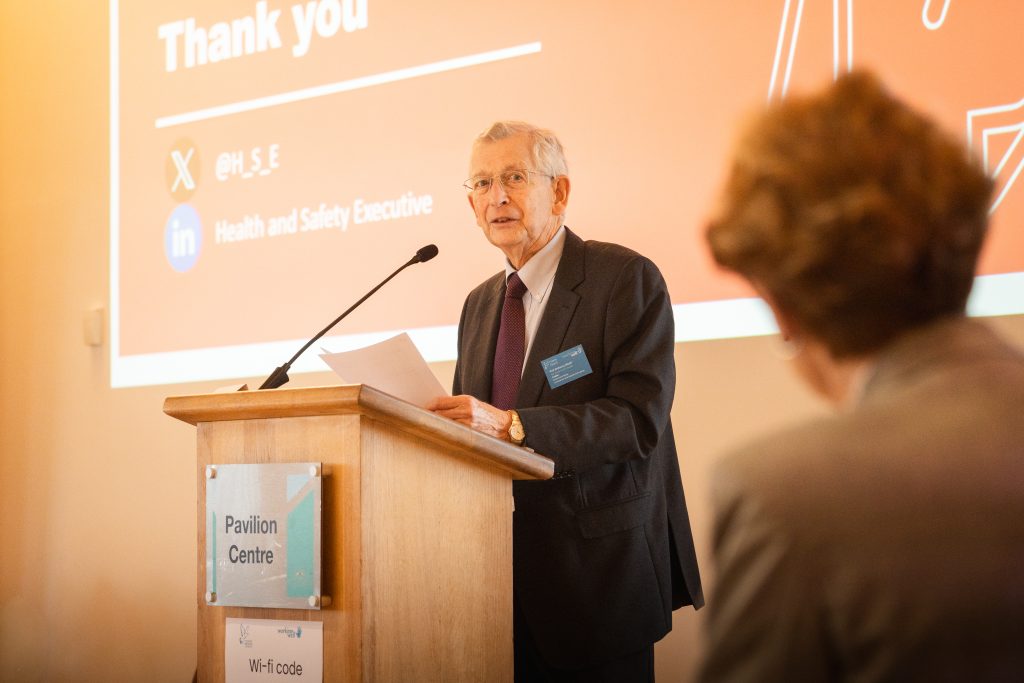 An image of Professor Tony Woolf stood behind a lectern, speaking at a conference