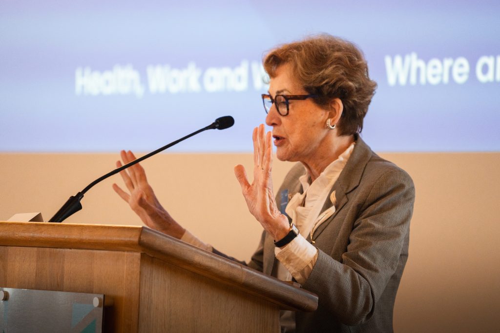 An image of Dame Carol Black stook behind a lectern, speaking at a conference