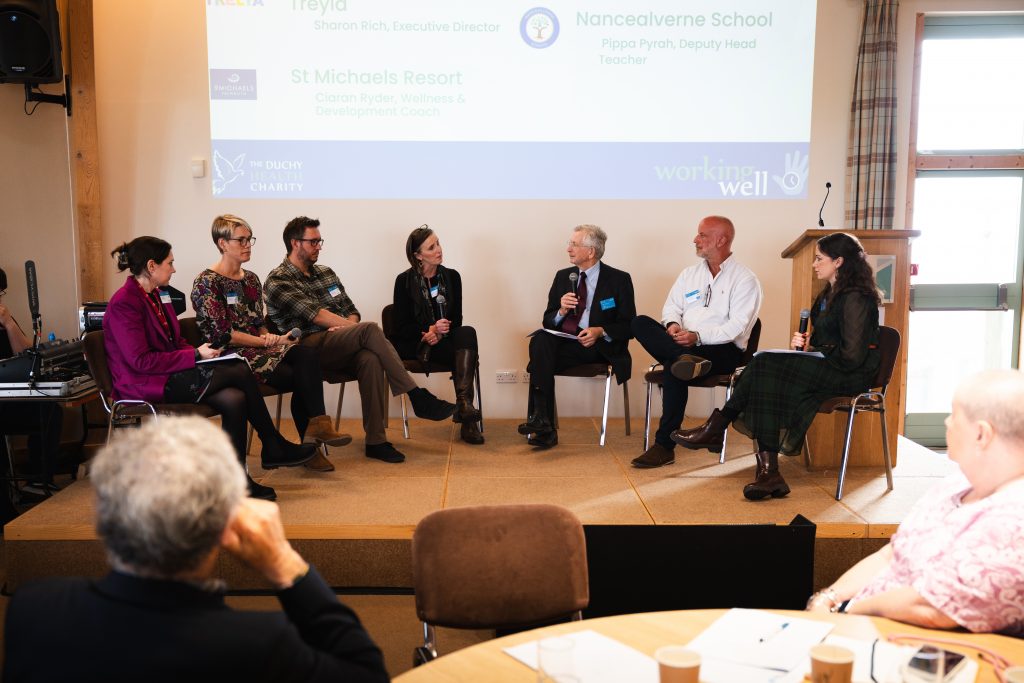 An image of people sat in chairs below a presentation screen in the form of a 'fireside chat'