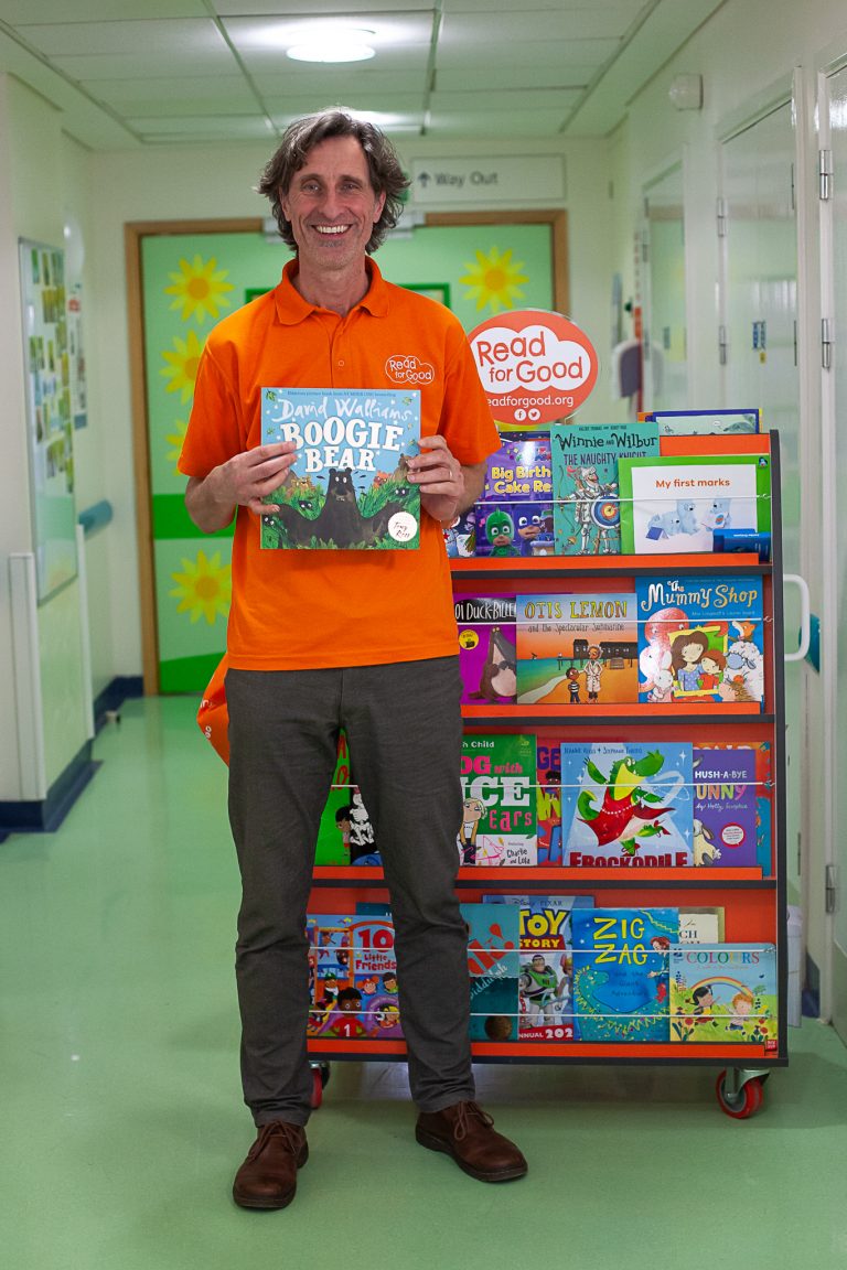 Michael Loader, Read for Good's storyteller standing in front of a mobile bookcase, holding a Boogie Bear book.